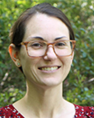 smiling woman with brown hair and glasses in front of greenery