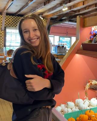 woman smiling while crossing arms and standing in front of mini pumpkins