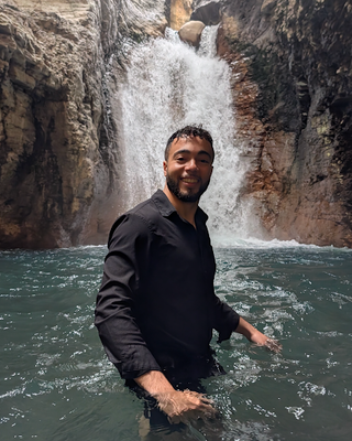 man standing in water with a waterfall in the background