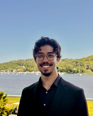 man with dark hair, glasses, and facial hair standing in front of a lake