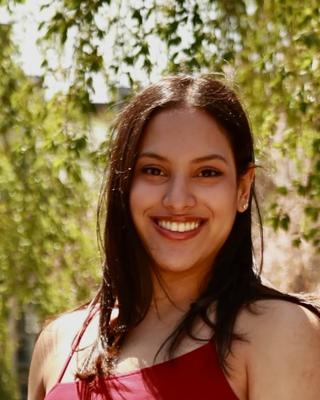 headshot of woman with dark hair smiling in front of a tree