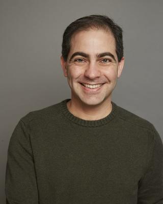 Head shot of man with dark hair, wearing a green sweater, and smiling