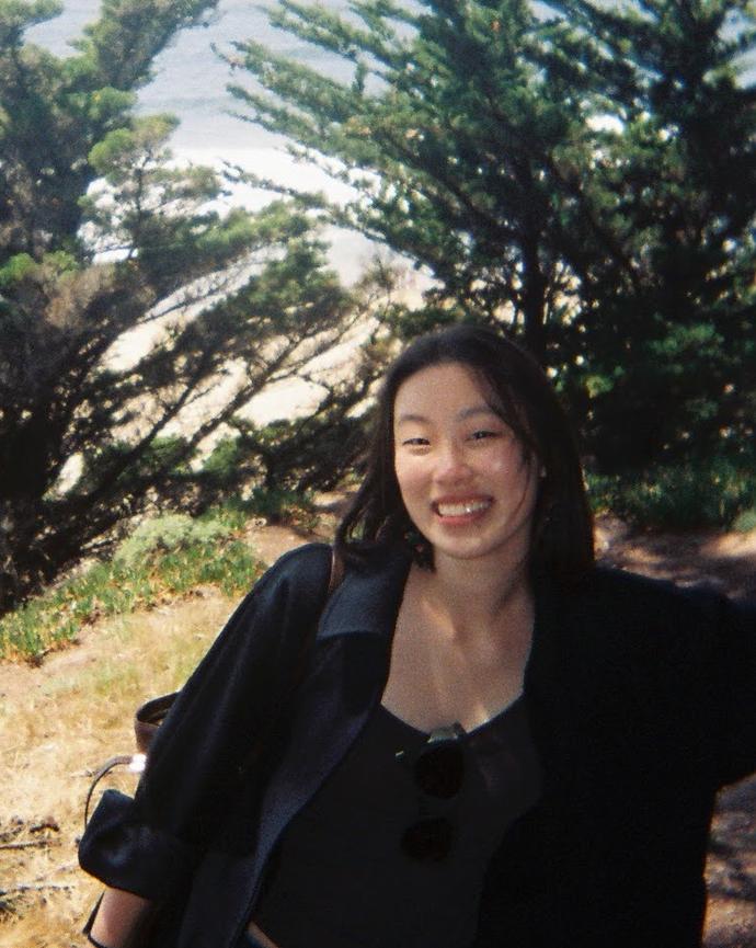 woman with dark hair standing in front of trees on a cliff side